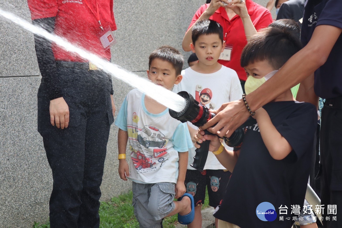 消防員指導低年級的學童體驗操作消防水槍。