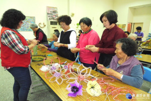 一群社區婆婆媽媽跟著藝術家王薰苹學作鋁線花、絲襪花、各色鋁線依序纏繞創作藝品。(記者/黃芳祿攝)