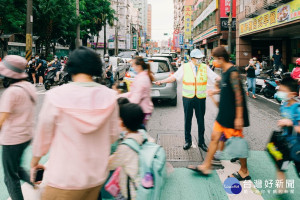 桃園市長鄭文燦穿著反光背心、手拿導護旗幟，在錦興國小校門口擔任一日導護志工，引導學童們過馬路、安全進入校園。